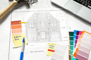 Blue prints for a custom home on a desk surrounded by a laptop and other various items