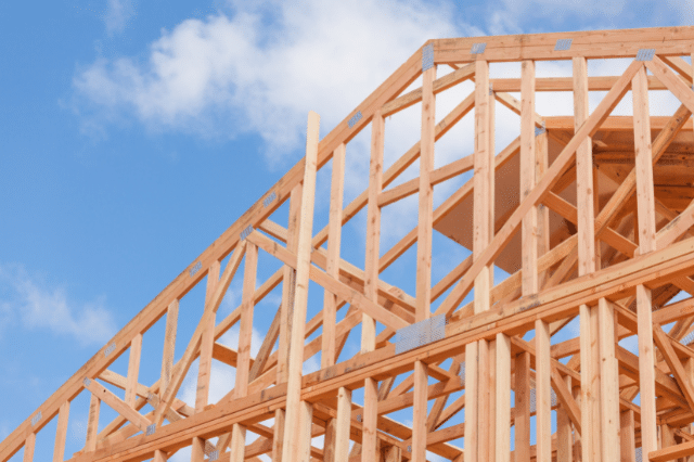 Close up of a frame of a house being built, against a blue sky.
