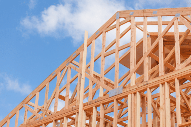 Close up of a frame of a house being built, against a blue sky. 
