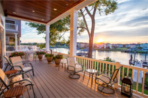 An elevated deck with tables, chairs, and plants overlooks fresh water at sunset.